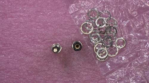 Two small metal hardware components and a pile of silver metal rings laid on a textured pink surface with some clear plastic wrapping visible.